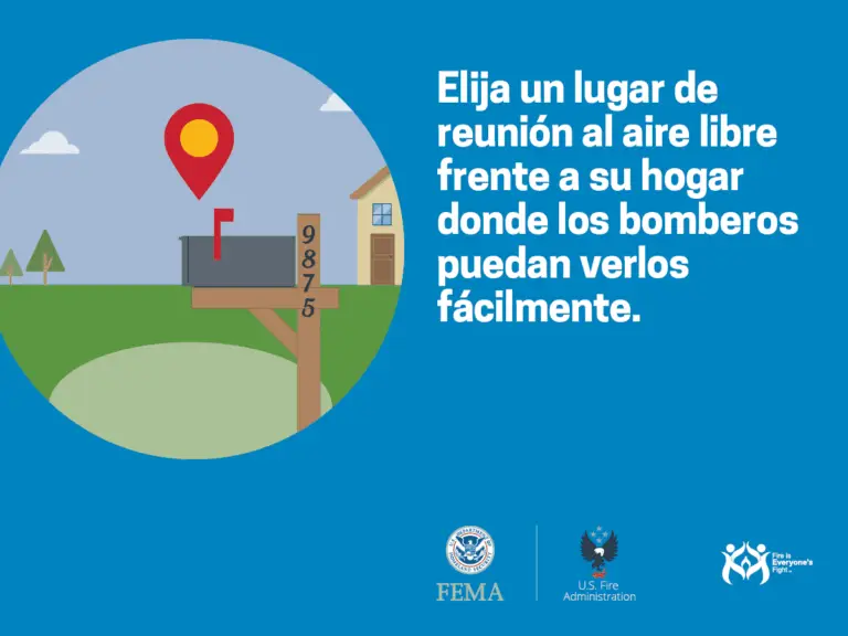 Imagen ilustrativa que promueve la seguridad, mostrando un punto de reunión al aire libre marcado con un icono de localización rojo para facilitar la visibilidad de los bomberos, con texto en español que aconseja seleccionar un lugar de reunión visible para los servicios de emergencia. logotipos de fema y us fire administration están presentes en la parte inferior.