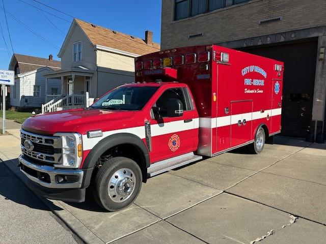 A red and white City of Reading Fire Rescue ambulance is parked outside a brick building on a sunny day, with residential houses visible in the background.